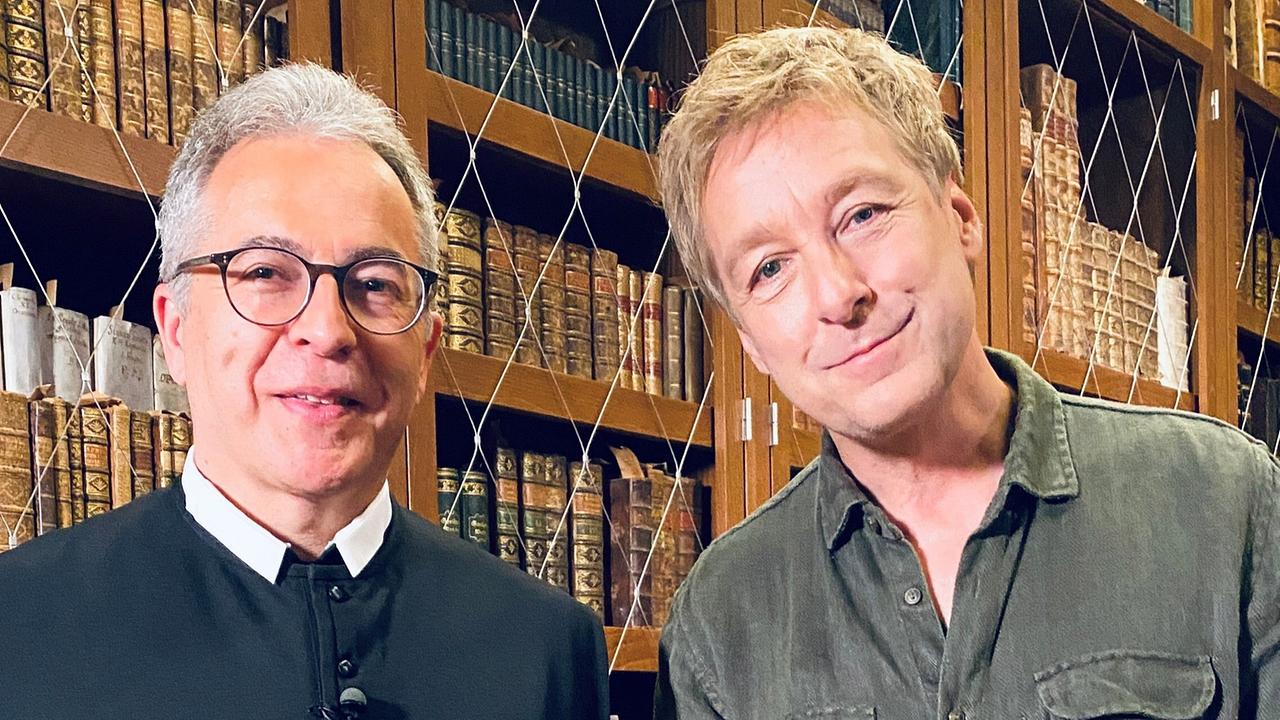 © ORF/Landesstudio Kärnten Max Müller und Pater Gerfried, Musuemsleiter Stift St. Paul stehen vor historischen Bücherregalen.