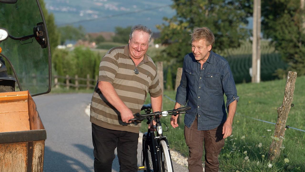© ORF/Landesstudio Kärnten Josef Raß und Max Müller gehen mit einem Fahrrad auf einem ländlichen Weg in Pölling.