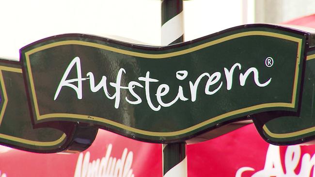 Ein grünes, goldgerahmtes Schild mit der Aufschrift „Austeirern“ an einem schwarz-weiß gestreiften Ständer.