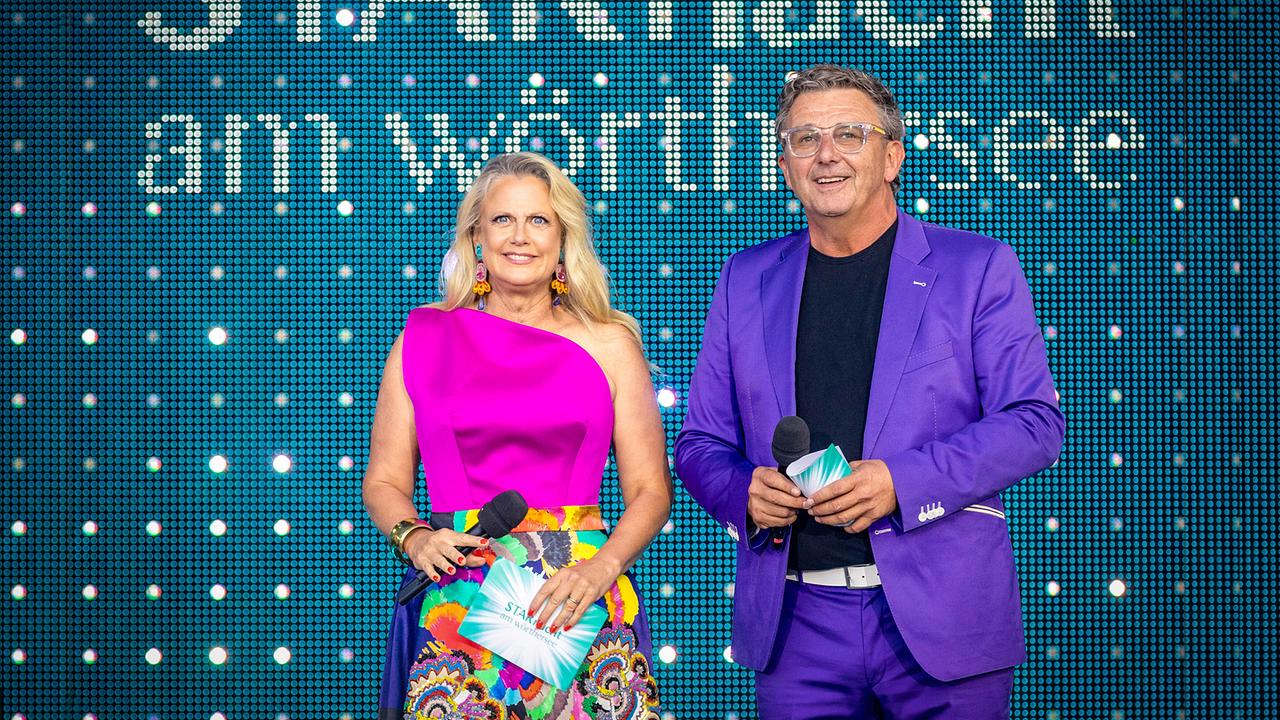 © ORF/ip|media/Peter Krivograd Barbara Schöneberger in einem pinken Oberteil mit bunt gemustertem Rock und Hans Sigl in einem violetten Anzug stehen vor einer leuchtenden Bühne mit der Aufschrift „STARnacht am Wörthersee“