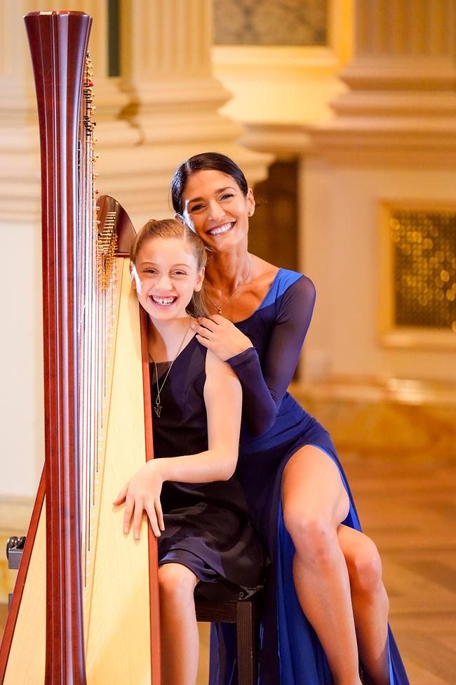 Aryana Devine und Ketevan Papava sitzen lächelnd und elegant gekleidet neben einer Harfe in einem elegant gestalteten, festlichen Raum.