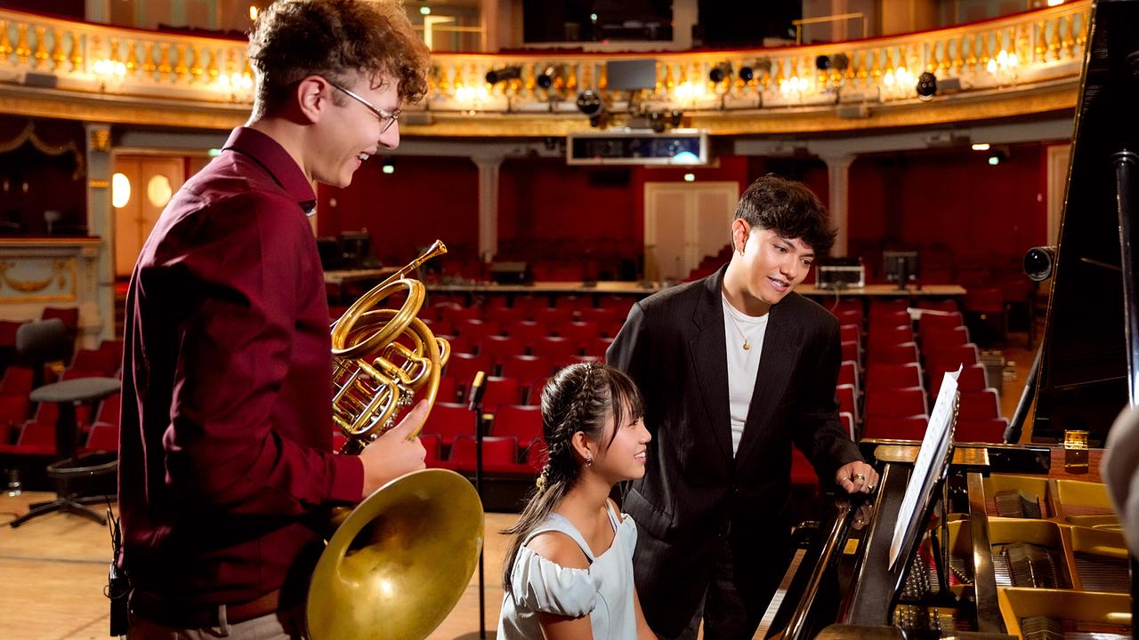 Julius Constantin Schantl mit Oboe, Sona Tamura am Klavier und JJ, der daneben steht, auf einer Bühne in einem prunkvoll dekorierten Saal