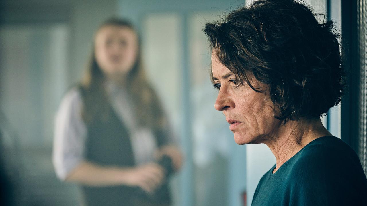 Kommissarin Lena Odenthal blickt nachdenklich nach unten im Kommissariat, im Hintergund unscharf ihr Kollege Nico.