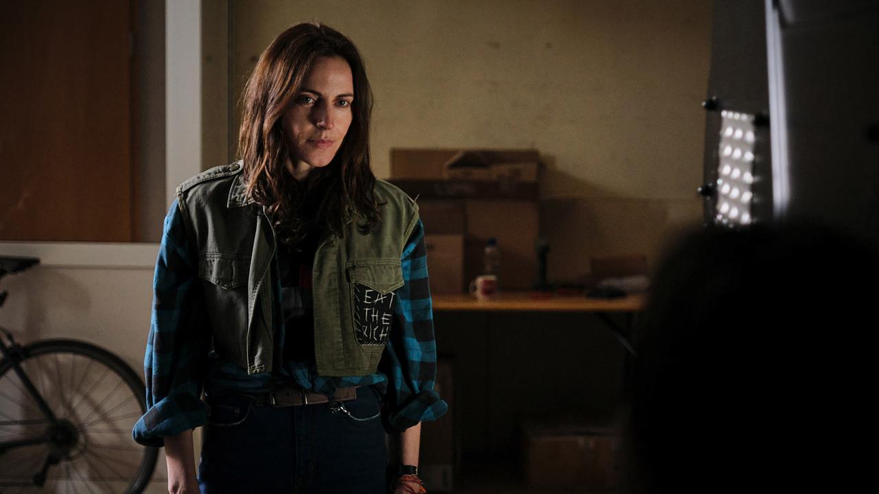 Zoe steht in einem spärlich beleuchteten Raum einer Kollegin gegenüber.