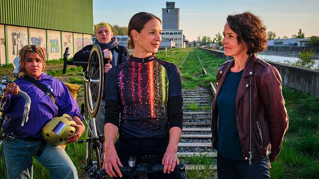 Zwei Fahrradfahrer von Velopunks, Johanna Stern, die undercover ermittelt, und Lena Odenthal stehen neisammen auf stillgelegten Gleisen in einem industriellen Umfeld neben dem Rheinufer.