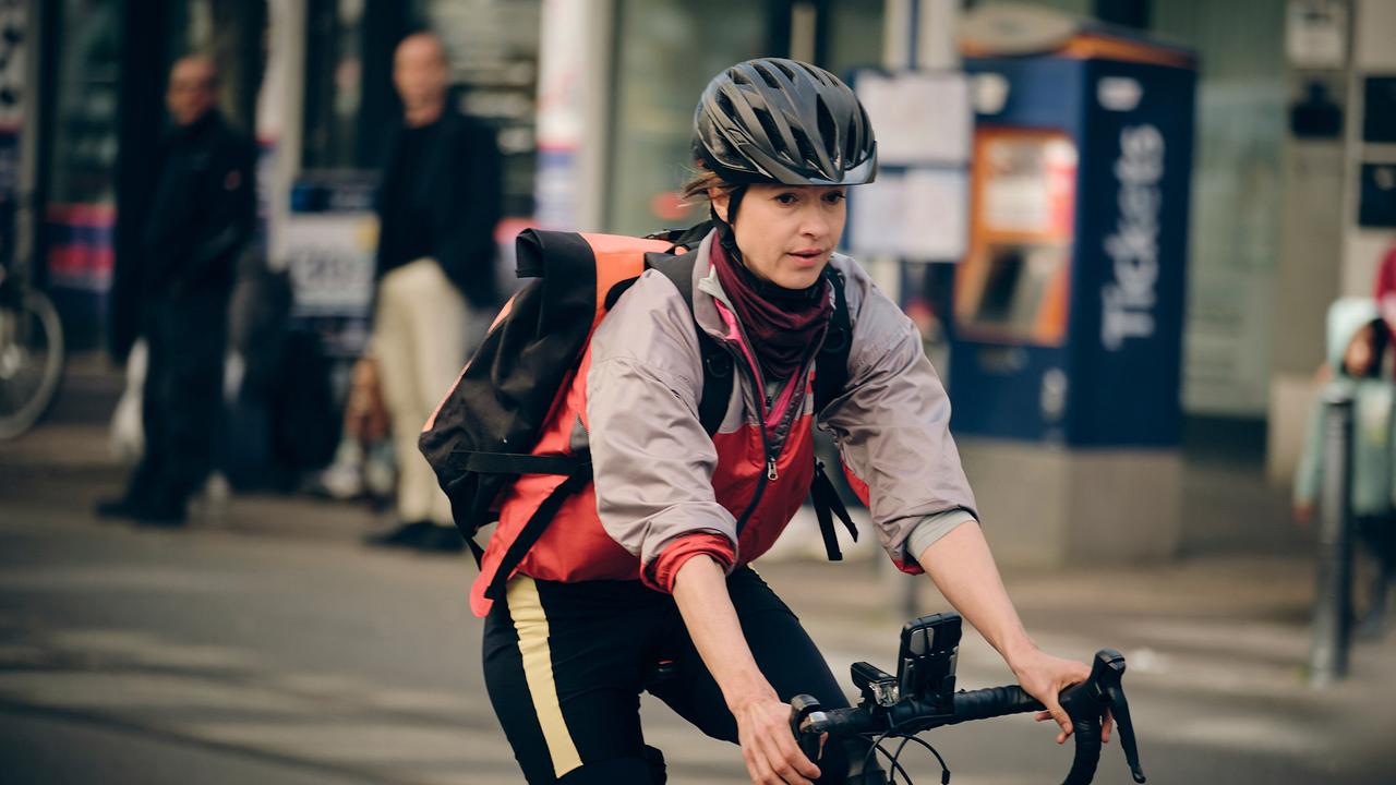 Johanna Stern strampelt sich als verdeckt ermittelnde Fahrradkurierin ab und fährt durch eine Stadtstraße, ausgerüstet mit Helm, Rucksack und sportlicher Kleidung.