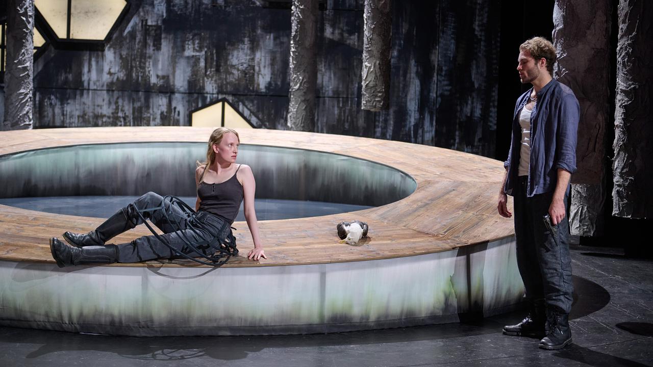 Auf der Bühne sitzt Stella Papst auf einem runden, ringförmigen Podest, während Carl Silberman danebensteht.