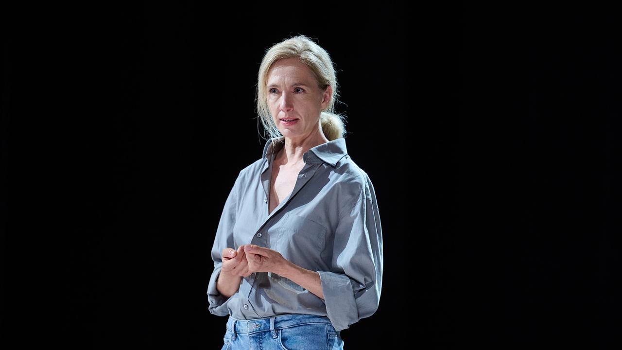 Gina Rohland in grauem Hemd und Jeans steht im Scheinwerferlicht vor schwarzem Hintergrund auf der Bühne bei der Probe.