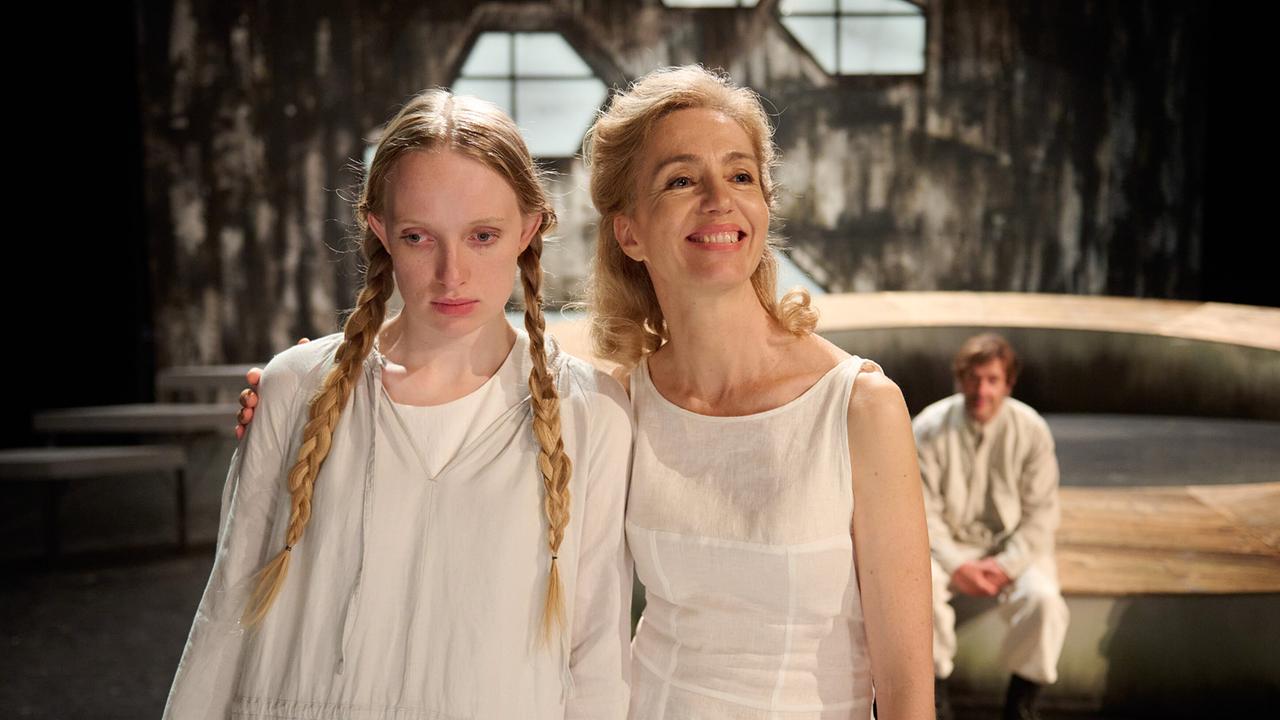 Stella Papst als Masha, Gina Rohland als Arkadina , beide in hellen Kleidern stehen eng beieinander auf einer Bühne, im Hintergrund sitzt Johannes Lange als Ssorin.