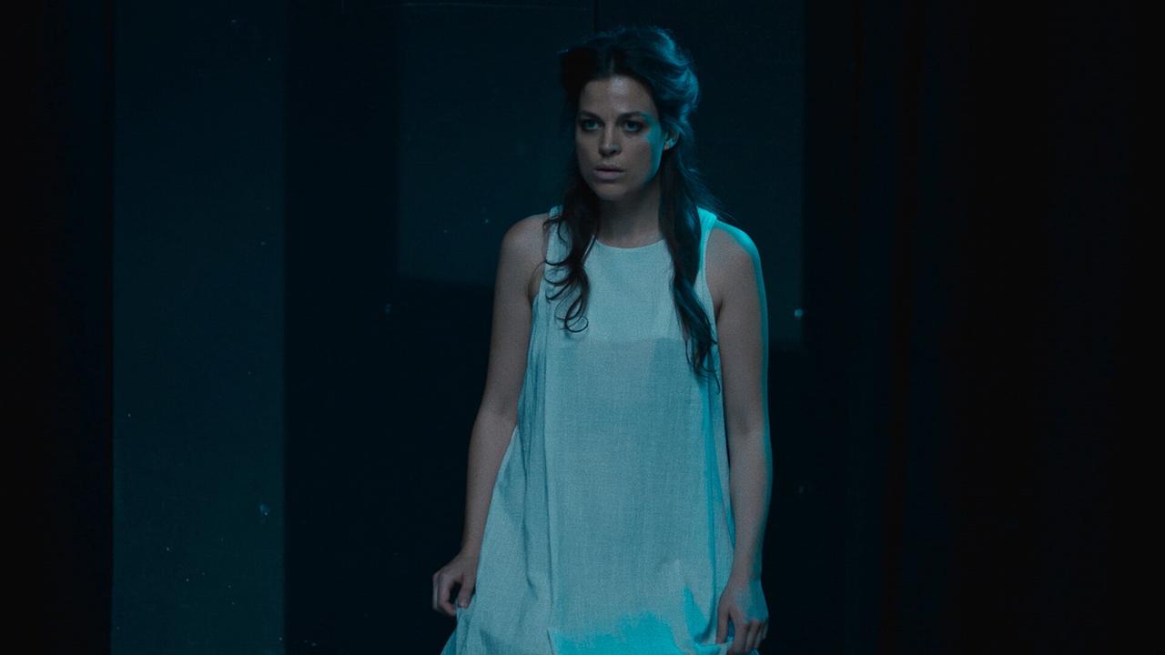 Nora Nielsen in einem weißen, luftigen Kleid auf der Bühne in der Rolle der Nina vor dunklem Hintergrund.