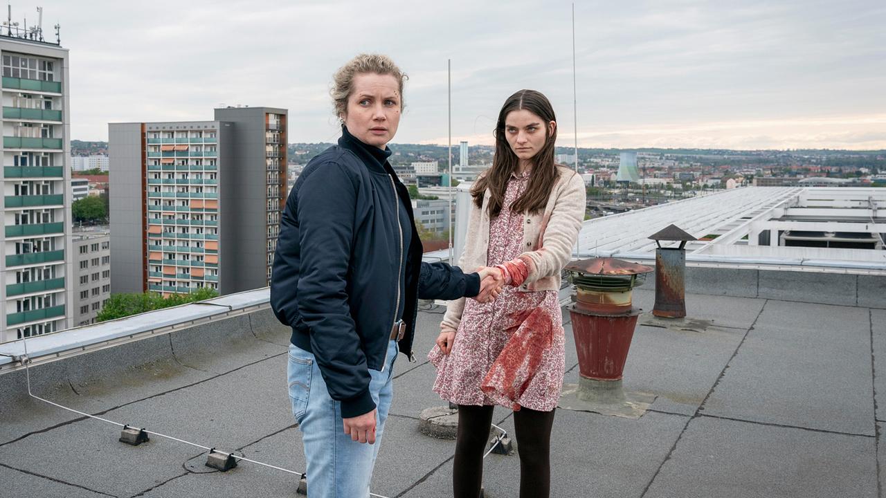 Leonie Winkler findet die verletzte Amanda auf einem Flachdach mit Rundumblick auf die Stadt bei bewölktem Wetter.
