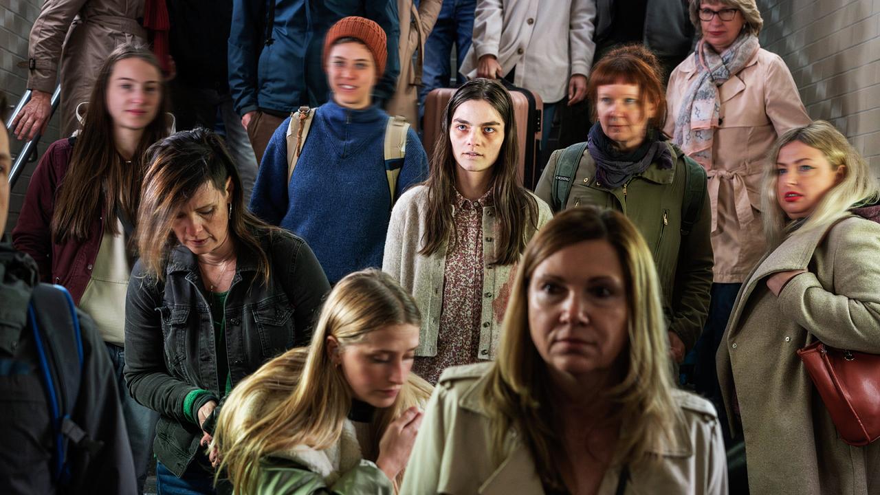 Amanda steht inmitten einer Menge von Passanten am Bahnhof