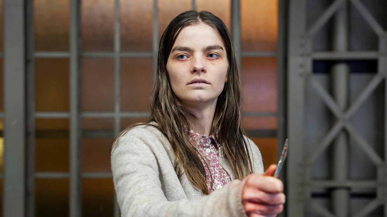 Amanda steht kreidebleich mit einem Skalpell in der Hand am Bahnhof.