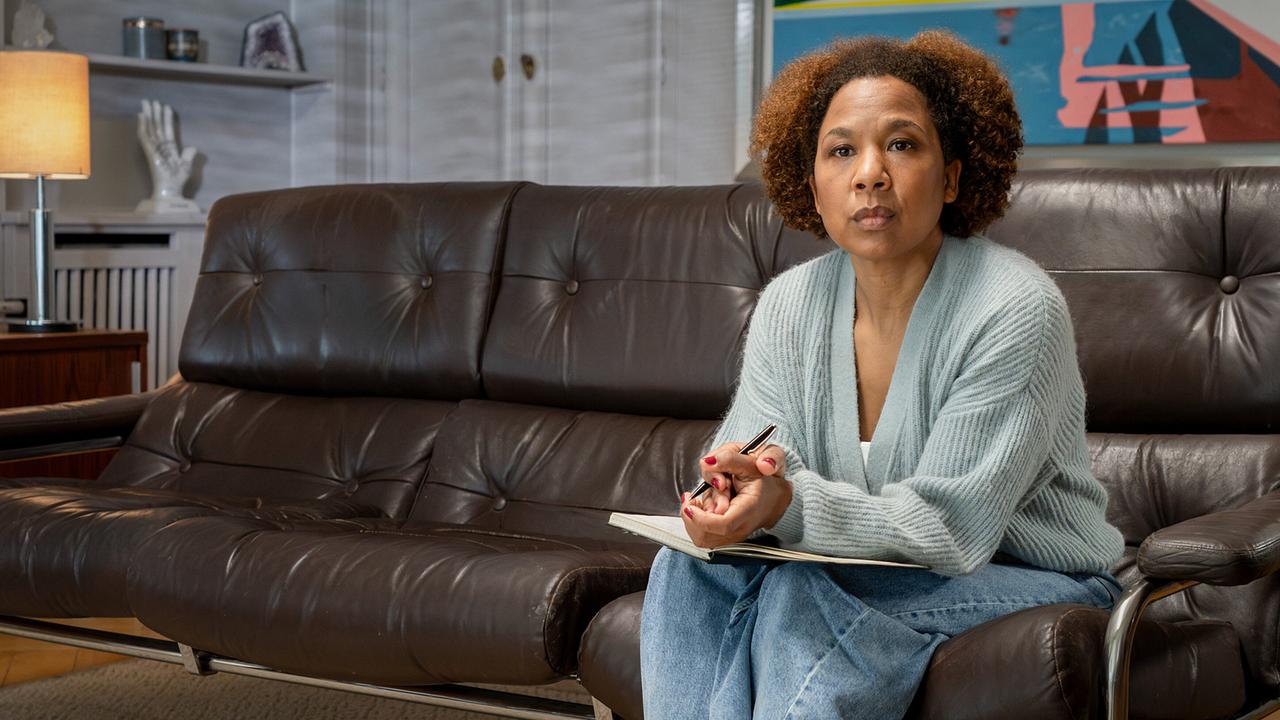 Dr. Gülsüm Diallo sitzt mit Notizbuch auf ihrem Schoß auf einer braunen Ledercoach im Besprechungszimmer