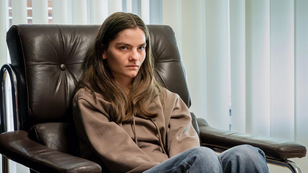 Die Jugendliche Amanda sitzt in einem Besprechungszimmer in einem großen Ledersessel, in sich zusammengesunken und nachdenklich.