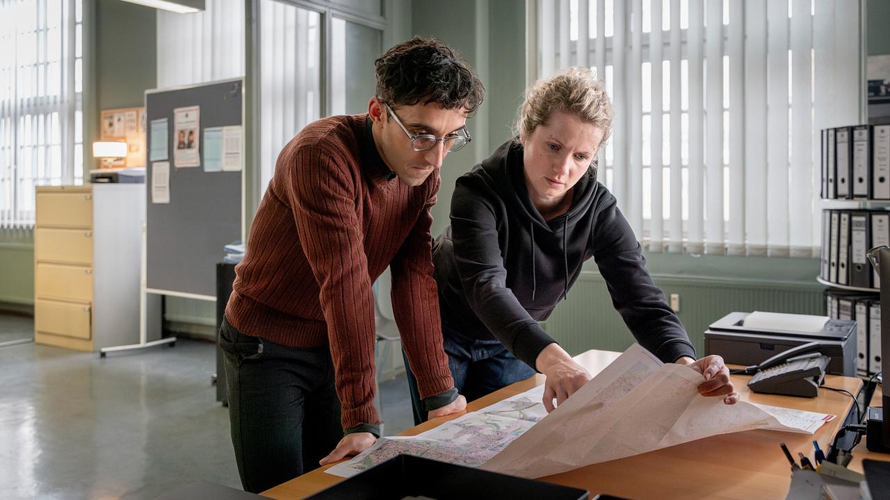 Philipp Laupheimer und Leonie Winkler beugen sich am Schreibtisch über eine Karte der Stadt Dresden im Kommissariat.