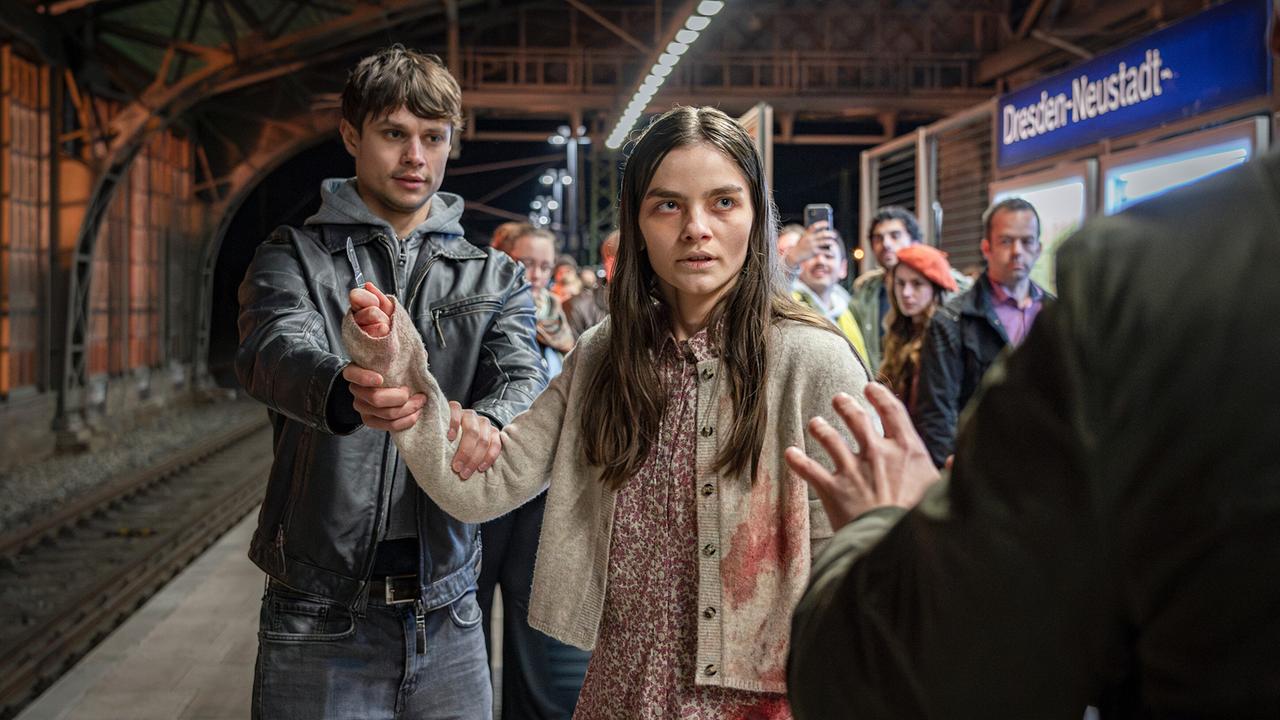 Am Bahnsteig „Dresden-Neustadt“ wird die am Arm verletzte Amanda mit einem Skalpell in der Hand von Passanten überwältigt.