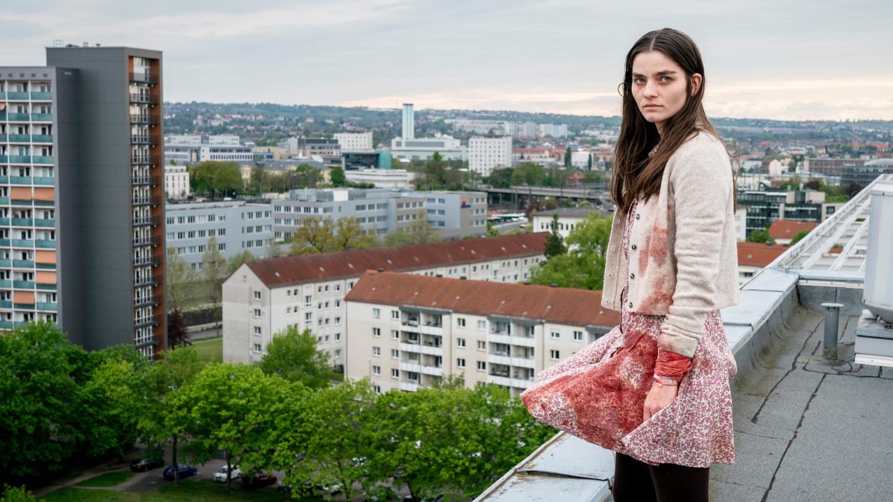 Amanda steht blutverschmiert auf einem Flachdach eines Gebäudes, sie sucht ihre Schwester Jana.