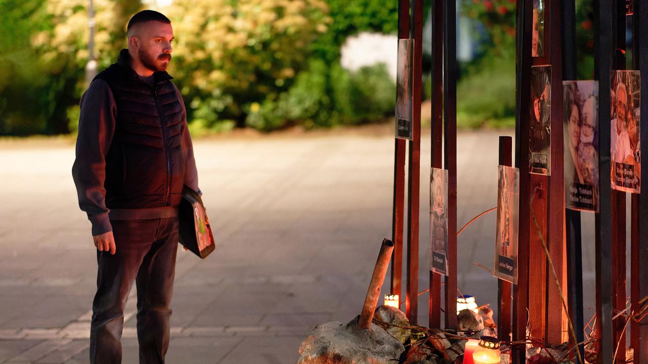 Hamza Kulina steht abends vor einer Gedenkstätte mit Kerzen und Fotos im Freien.