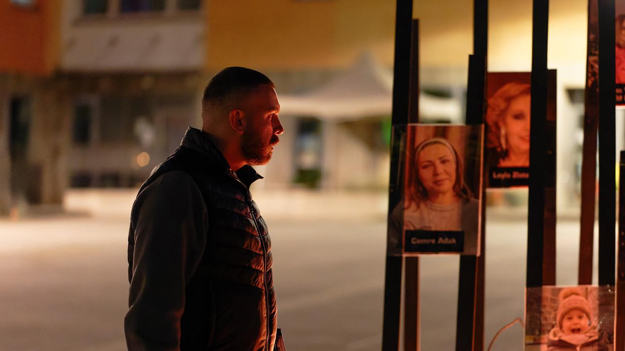 Hamza Kulina betrachtet abends vor einer Wohnhausanlage die Namen und Bilder an einer beleuchteten Gedenkinstallation.