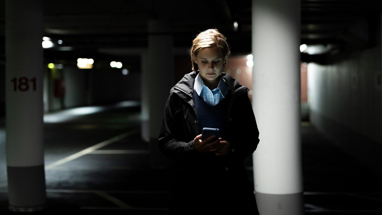 In einer dunklen Tiefgarage steht Andrea Hofer allein zwischen Betonpfeilern und blickt auf ein Smartphone.