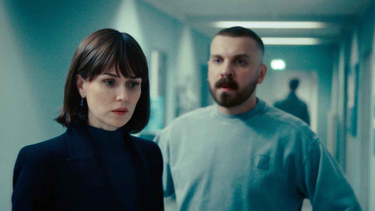 In einem verschwommenen Flur stehen Maryam Azadi und Hamza Kulina  nebeneinander, während im Hintergrund eine weitere Person den Flur entlanggeht.