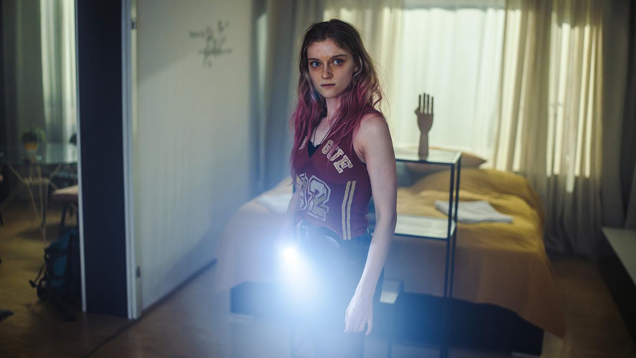 Kara Roth steht mit einer eingeschalteten Taschenlampe in einem abgedunkelten Schlafzimmer in der Wohnung.