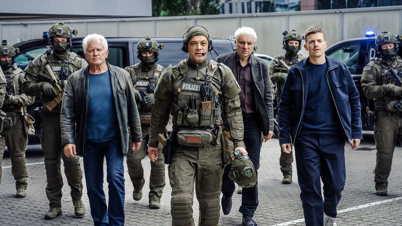 Ivo Batic, SEK Chef Buvak, Franz Leitmayr  und Kalli Hammermann und weitere Einsatzkräfte vor ihrem Einsatz am Klinikum auf einem Parkplatz.