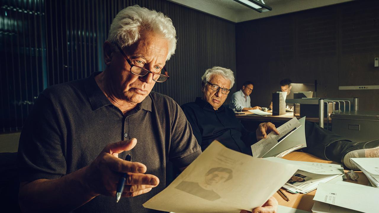 Ivo Batic und Franz Leitmayr durchsuchen nachts die Akten an ihren Schreibtischen im Büro.