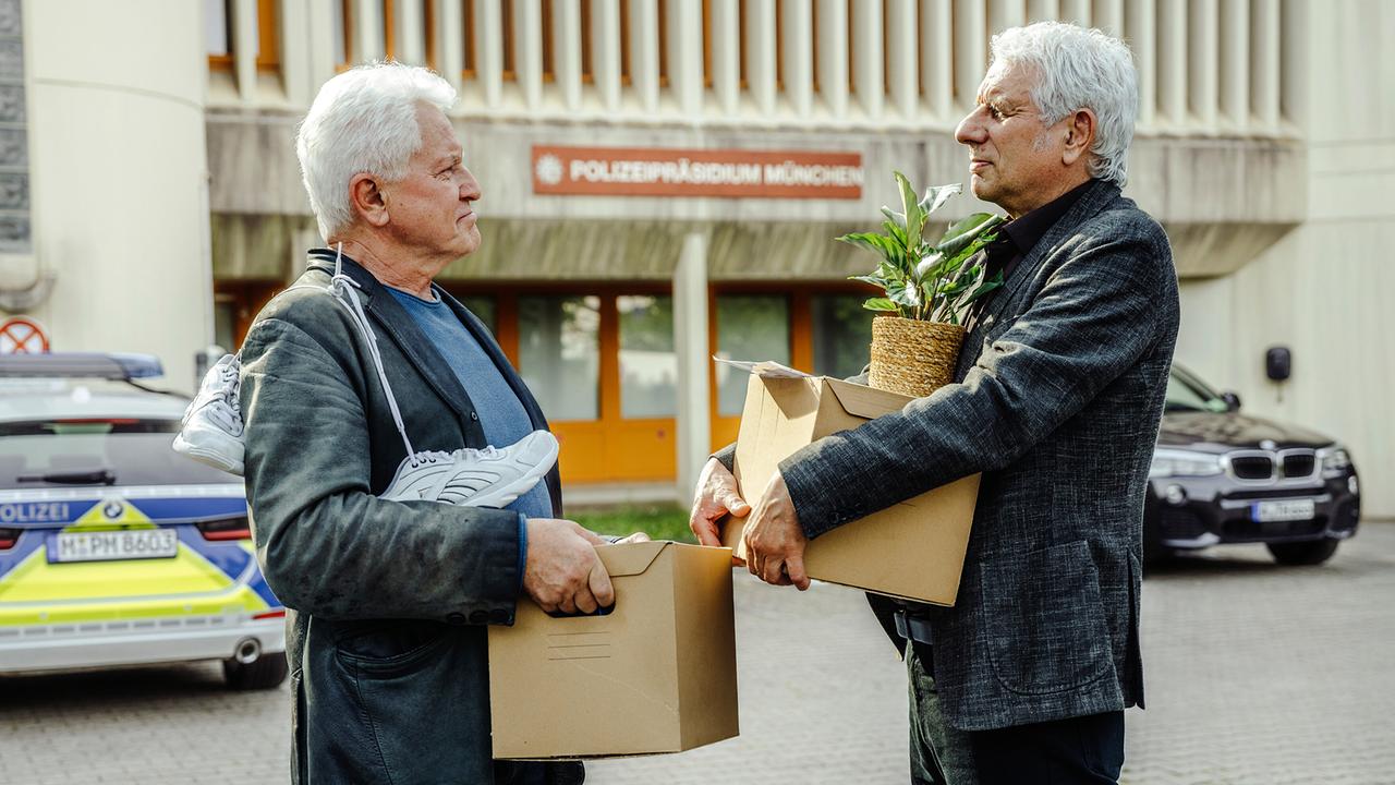 Ivo Batic und Franz Leitmayr stehen vor dem Präsidium mit Kartons mit persönlichen Gegenständen im Arm, um sich zu verabschieden.