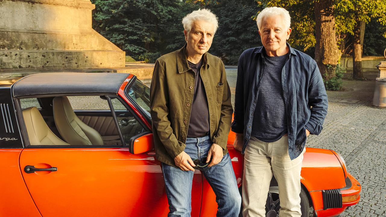 Franz Leitmayr und Kriminalhauptkommissar Ivo Batic lehnen an einem roten Sportwagen und posieren im Freien.