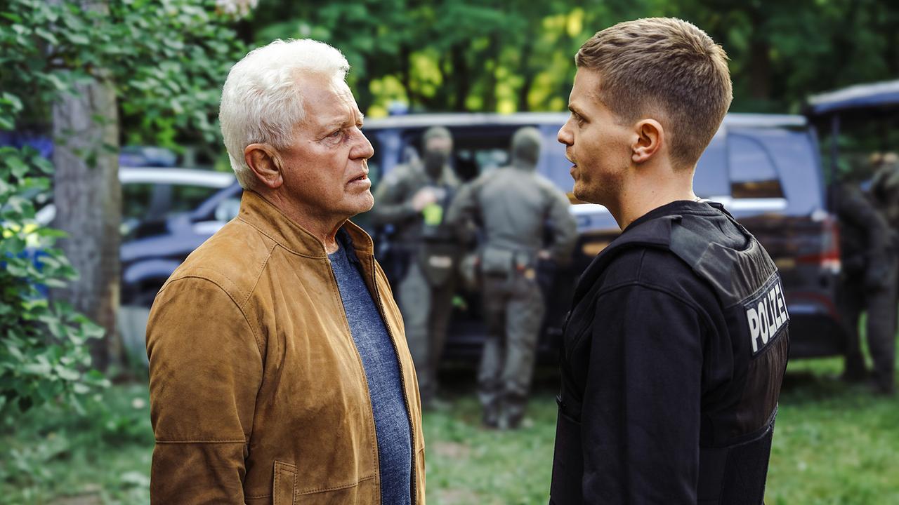  Ivo Batic und Kalli Hammermann stehen vor der Stauwehrhalle, im Hintergrund stehen weitere Einsatzkräfte bei Fahrzeugen.