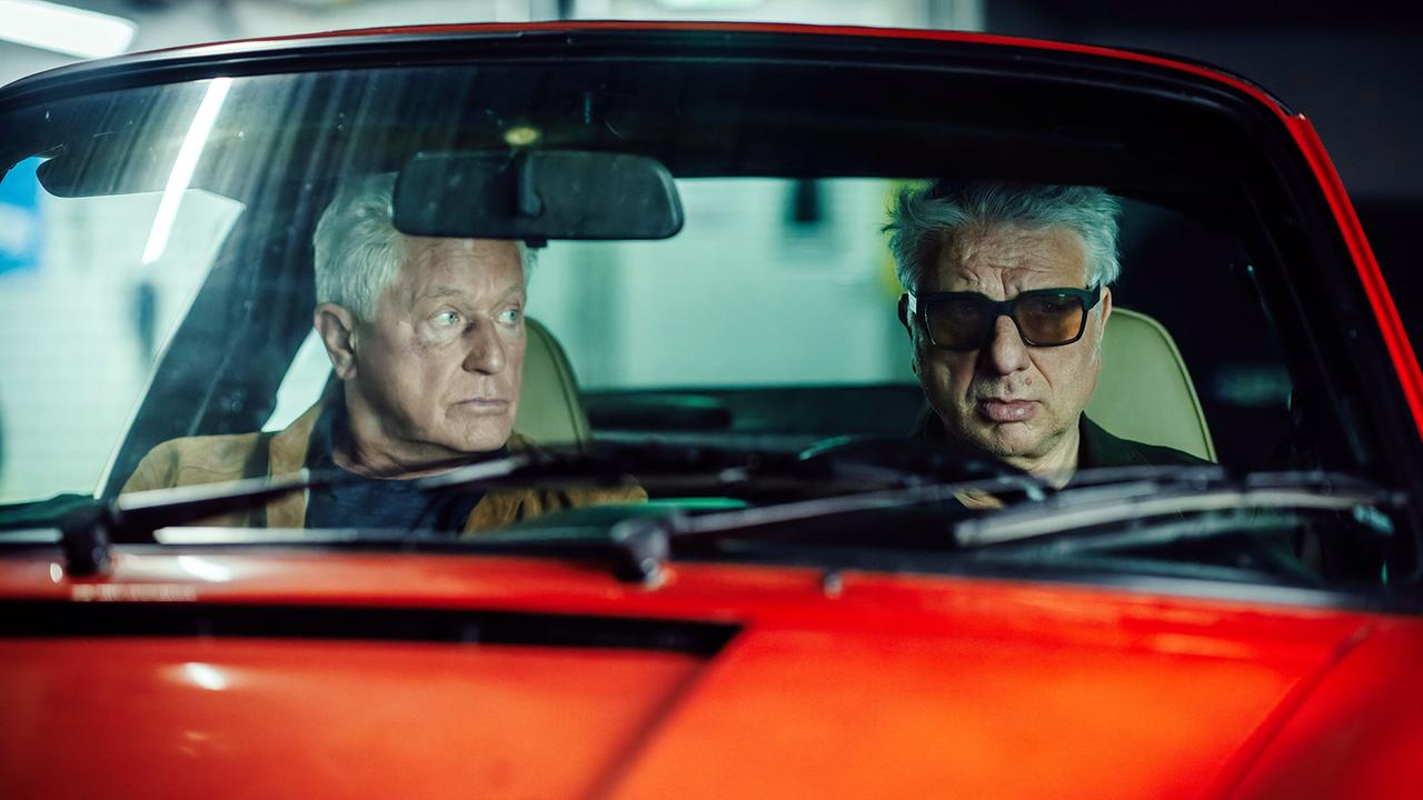  Ivo Batic und Franz Leitmayr sitzen im roten Porsche in der Tiefgarage und beobachten die Mitarbeiter von Prime Wave.