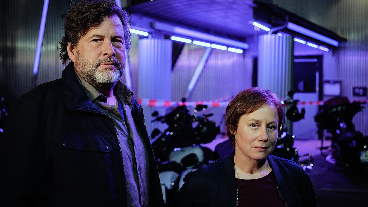 Friedemann Berg und Franziska Tobler stehen nachts vor dem abgesperrten Gebäude mit Motorrädern und auffälliger blauer Beleuchtung.
