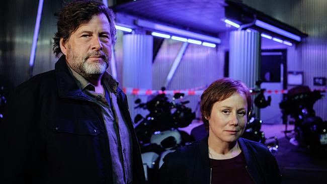 Friedemann Berg und Franziska Tobler stehen nachts vor dem abgesperrten Gebäude mit Motorrädern und auffälliger blauer Beleuchtung.