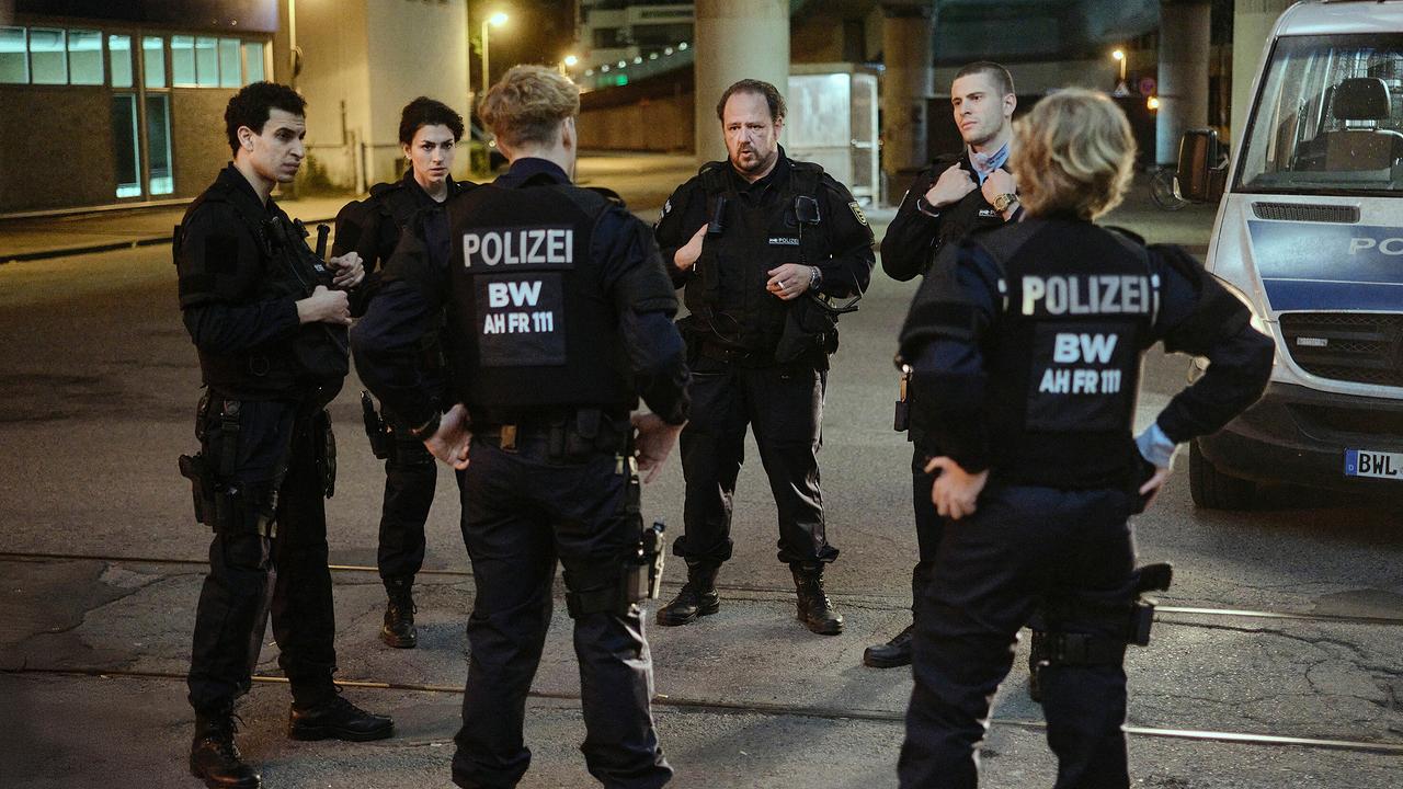 Sechs Polizeibeamtinnen und -beamte stehen nachts im Kreis auf einer Straße und besprechen etwas.