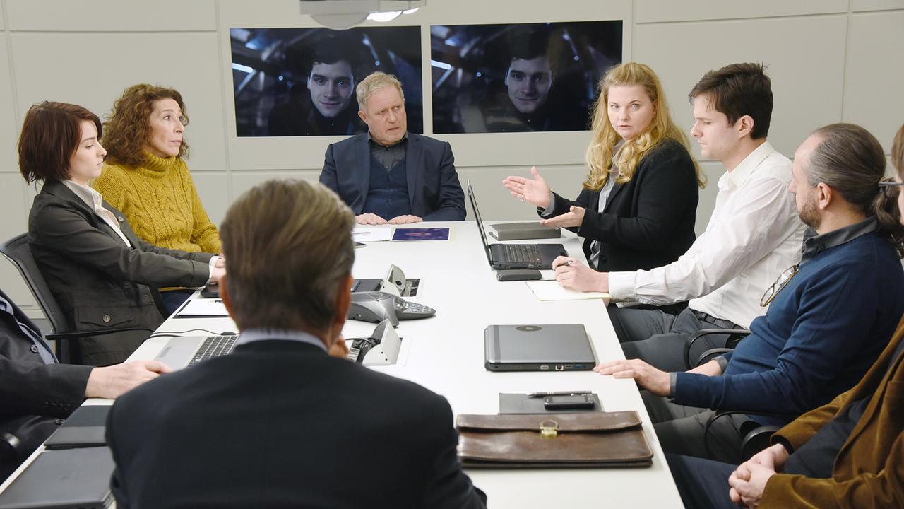 Mehrere Menschen unter ihnen Bibi Fellner, Moritz Eisner und Lisa Aichinger sitzen um einen Konferenztisch und besprechen die Lage. Im Hintergrund ist zweimal ein Foto von David Frank eingeblendet.