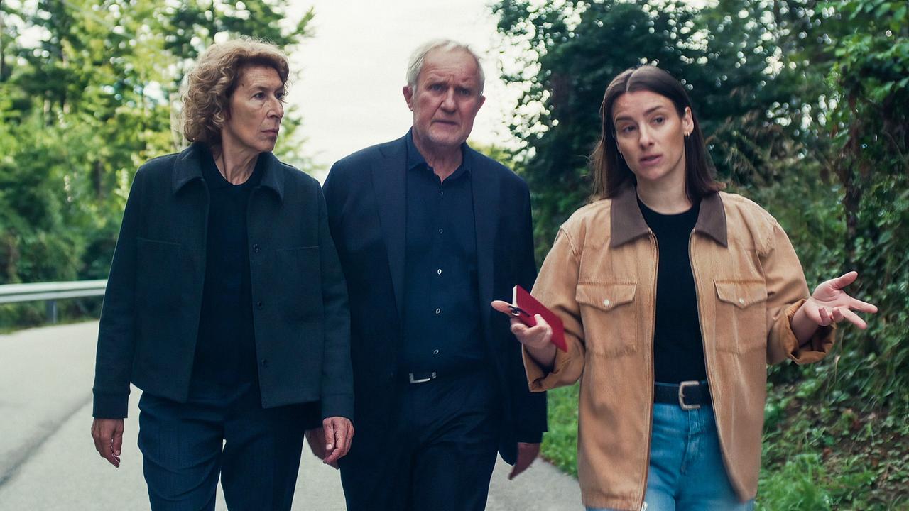 Bibi Fellner, Moritz Eisner und Meret Schande gehen gemeinsam auf einer ruhigen Straße im Grünen entlang und unterhalten sich.