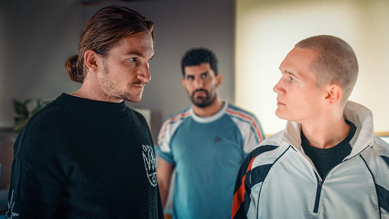 Simon Rechnik, Araz Barzani und Leon Prammer stehen in einem Raum einander angespannt gegenüber.