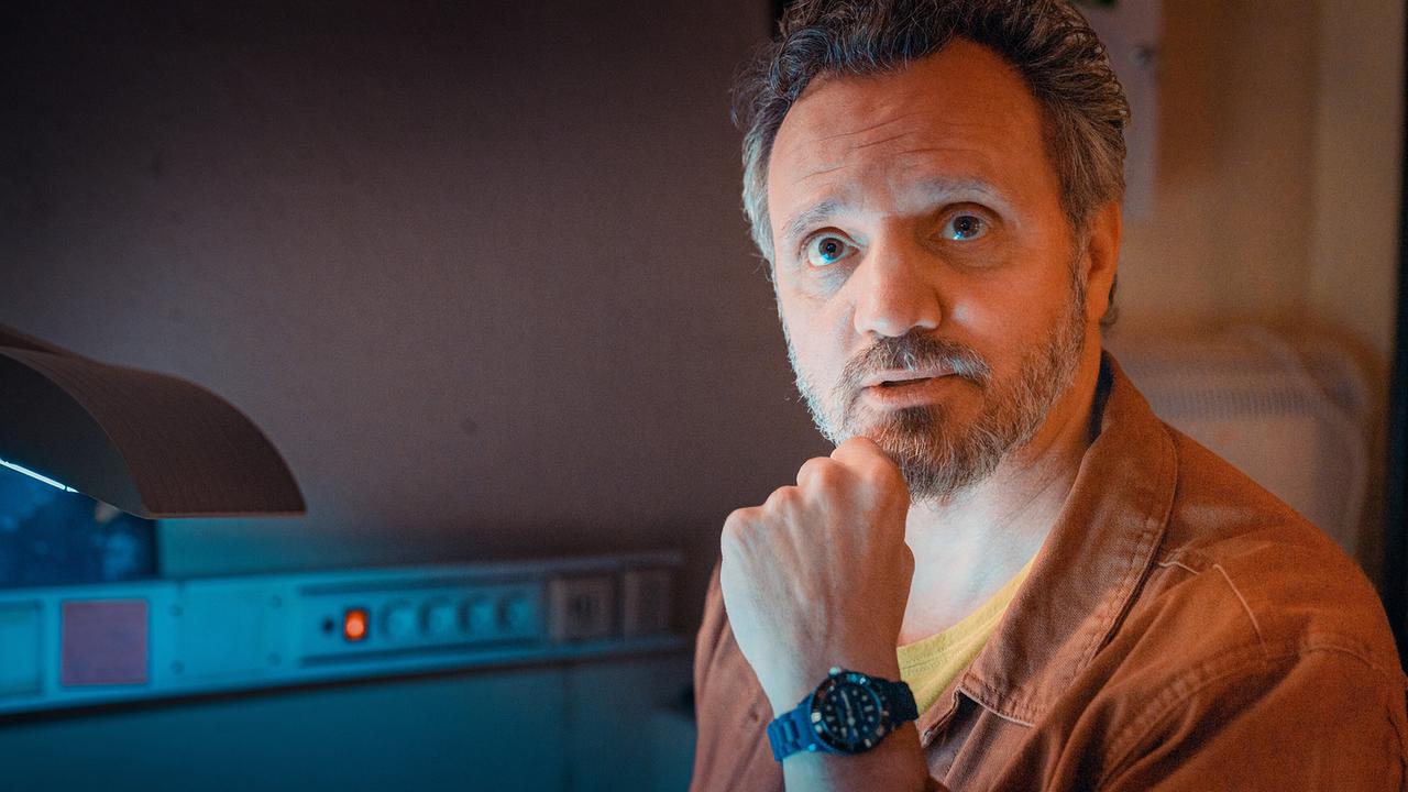 Nahaufnahme von David Walcher, der an einem Schreibtisch mit Tischlampe sitzt und seinen Kopf auf die Hand stützt.