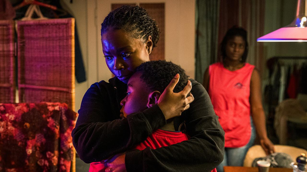Moya und Yaro müssen eine neue Unterkunft suchen: Moya umarmt Yaro fest, während Sanaa Mukambo weiter hinten im Raum steht.