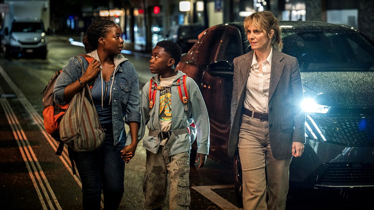 Moya Alemu, Yaro Alemu und Kommissarin Isabelle Grandjean gehen nachts auf einem Gehsteig, ein Auto mit eingeschalteten Scheinwerfern steht neben ihnen.