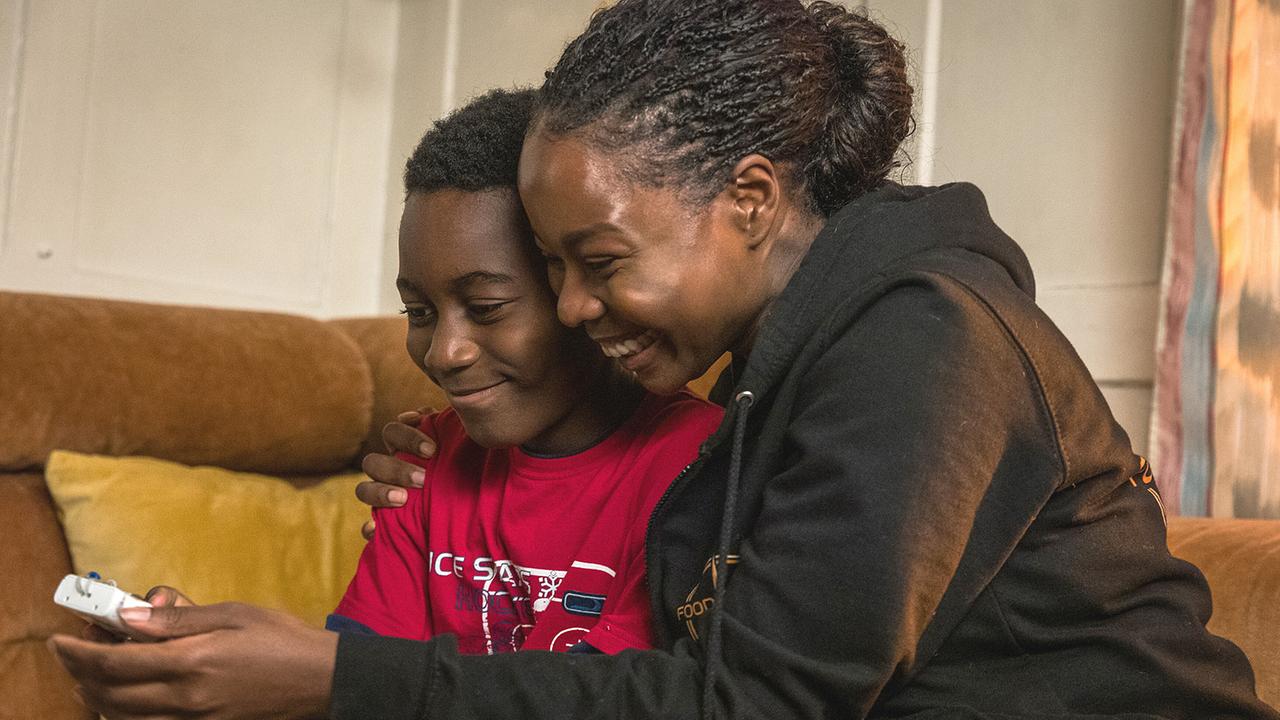 Moya Alemu sitzt mit Yaro auf einem Sofa, umarmt ihn und sie betrachten die Fotos, die Yaro gemacht hat.