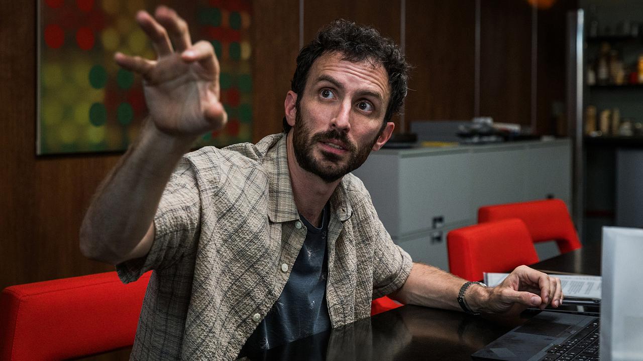 Lagebesprechung im Kommissariat: Noah Löwenherz  sitzt an einem Tisch und gestikuliert erköärend mit erhobener Hand.