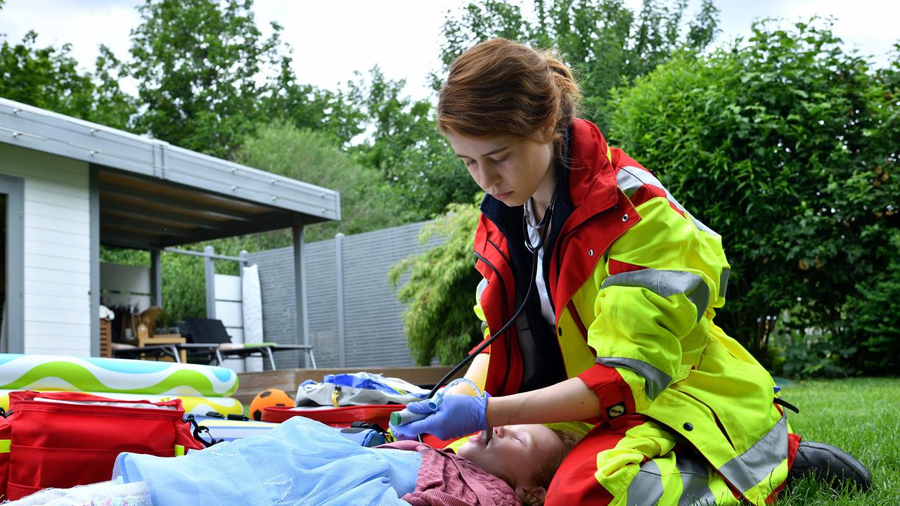 Sanitäterin Greta Blaschke versucht in einem Garten vor einem Einfamilienhaus das Leben von Schlüters Tochter zu retten, die keine Luft mehr bekommen hat.