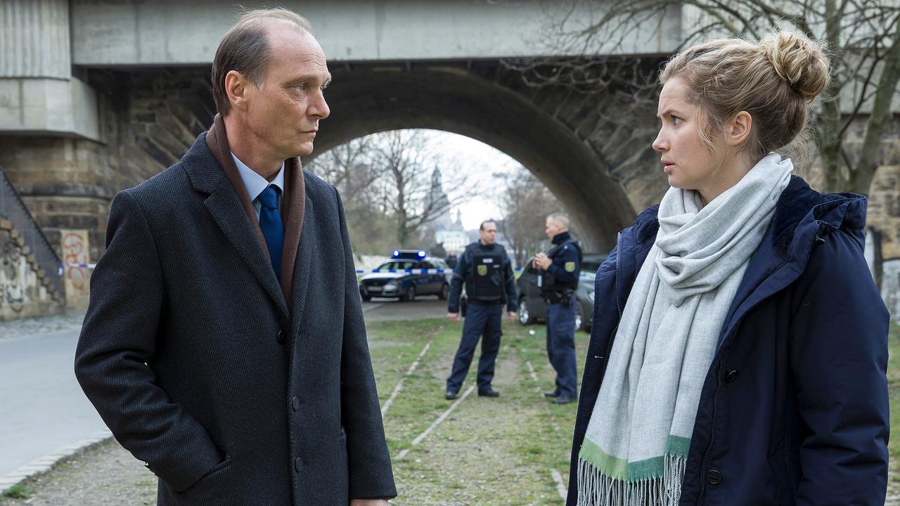 Peter Michael Schnabel und Leo Winkler am Tatort an den Elbbrücken, während Polizisten im Hintergrund den Bereich sichern.