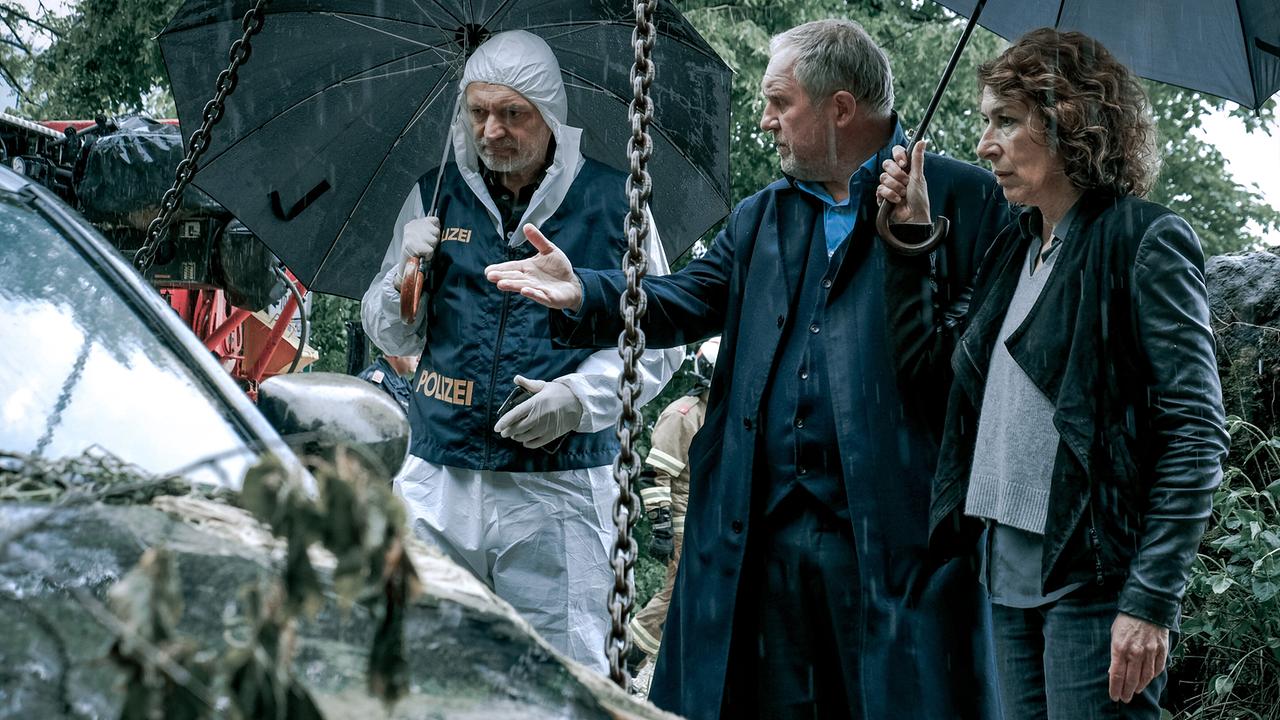 Im Regen begutachtet Spurensicherer Werner Kreindl mit Moritz Eisner und Bibi Fellner ein geborgenes Auto an einem Tatort im Wald.