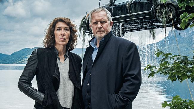 © ORF/Cult Film/Petro Domenigg Bibi Fellner und Moritz Eisner vor einem See, während im Hintergrund ein Auto aus dem Wasser gehoben wird.