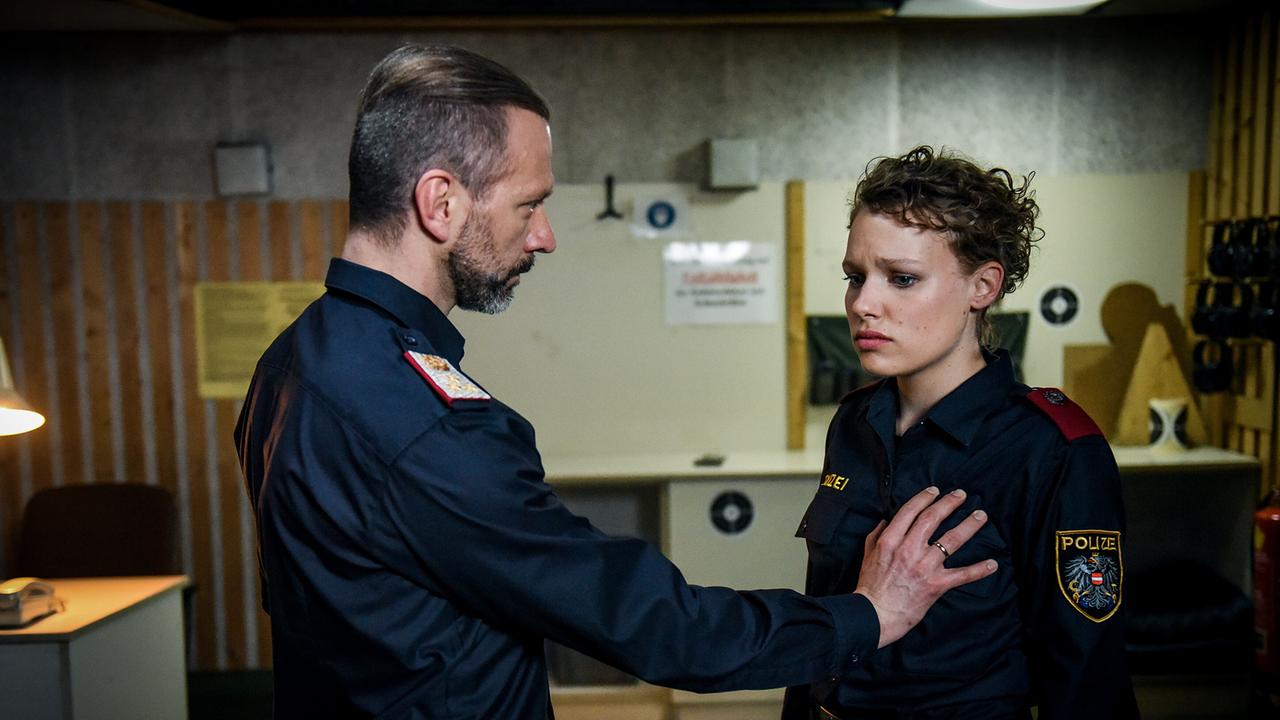 Der Polizeibeamte Thomas Nowak in Uniform spricht mit der jungen Kollegin Katja Humbold in einem Raum, wobei er eine Hand auf ihre Brust gelegt hat.