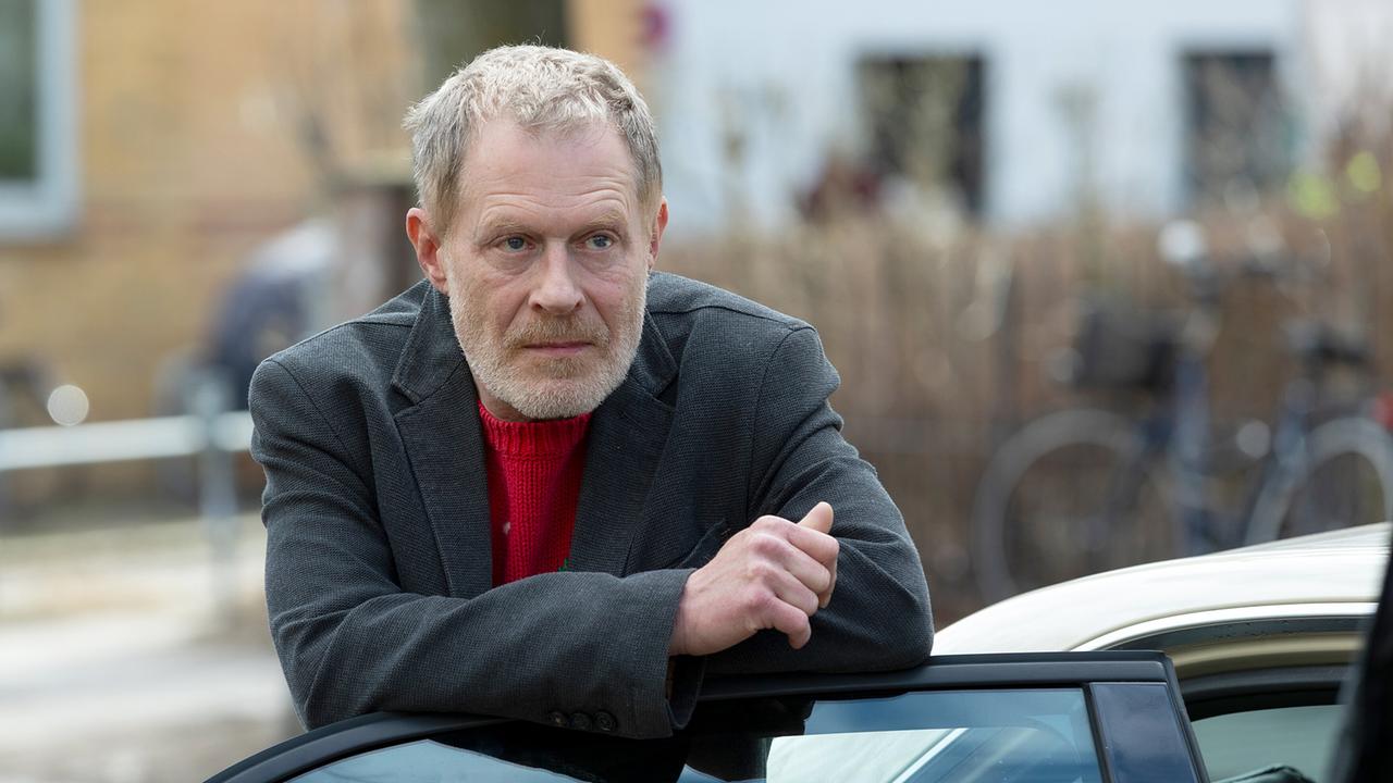 Der ernst blickender Matthias Vogel lehnt an der offenen Tür eines Autos im Freien.